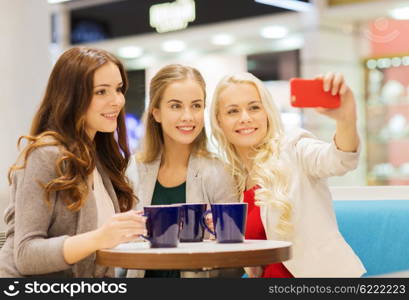 drinks, friendship, technology and people concept - happy young women with cups sitting at table and taking selfie with smartphone in cafe