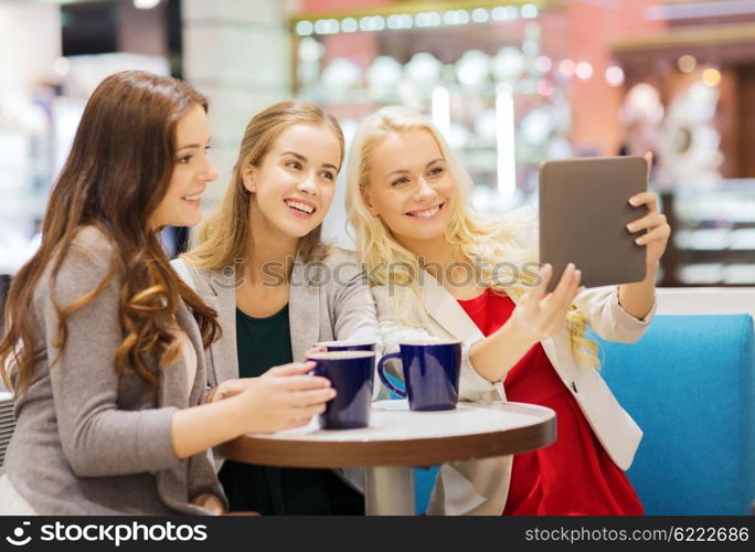 drinks, friendship, technology and people concept - happy young women with cups sitting at table and taking selfie with tablet pc in cafe