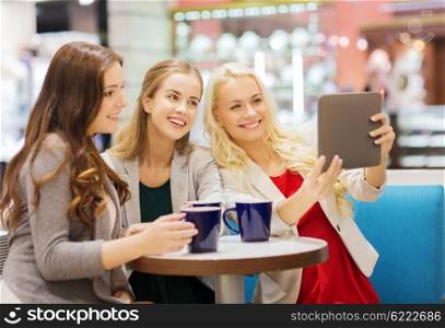drinks, friendship, technology and people concept - happy young women with cups sitting at table and taking selfie with tablet pc in cafe