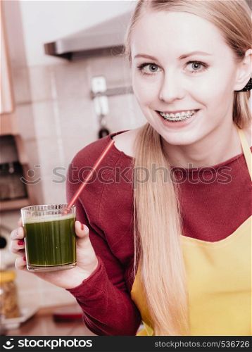 Drinks good for health, diet breakfast concept. Young woman in kitchen holding green healthy vegetable smoothie juice glass. Woman in kitchen holding vegetable juice