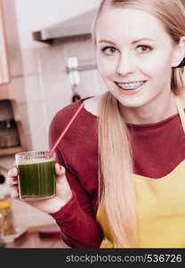 Drinks good for health, diet breakfast concept. Young woman in kitchen holding green healthy vegetable smoothie juice glass. Woman in kitchen holding vegetable juice