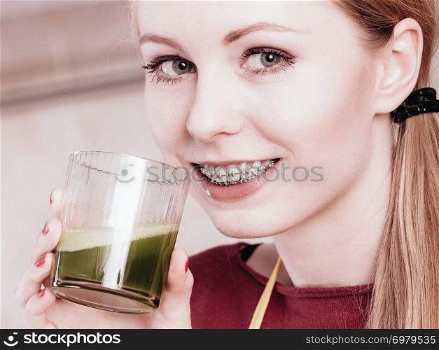 Drinks good for health, diet breakfast concept. Young woman in kitchen holding green healthy vegetable smoothie juice glass. Woman in kitchen holding vegetable smoothie juice