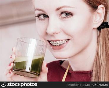 Drinks good for health, diet breakfast concept. Young woman in kitchen holding green healthy vegetable smoothie juice glass. Woman in kitchen holding vegetable smoothie juice