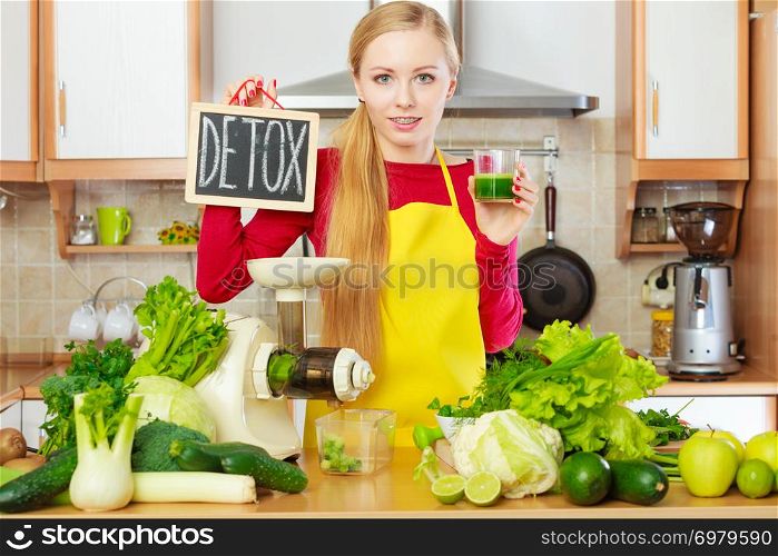 Drinks good for health, diet breakfast concept. Young woman in kitchen holding green healthy vegetable smoothie juice in glass next to detox sign.. Woman holding vegetable juice and detox sign