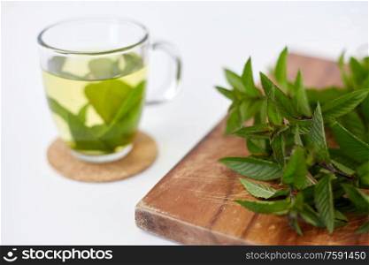 drinks, herbs and ethnoscience concept - herbal tea with fresh peppermint on wooden board. herbal tea with fresh peppermint on wooden board