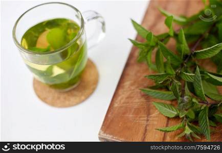 drinks, herbs and ethnoscience concept - herbal tea with fresh peppermint on wooden board. herbal tea with fresh peppermint on wooden board
