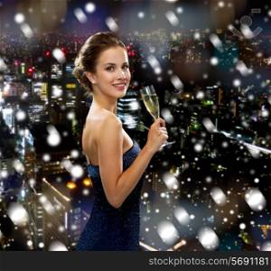 drinks, holidays, christmas, people and celebration concept - smiling woman in evening dress with glass of sparkling wine over snowy city background