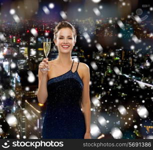 drinks, holidays, christmas, people and celebration concept - smiling woman in evening dress with glass of sparkling wine over snowy city background