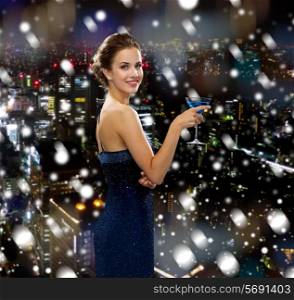 drinks, holidays, christmas, people and celebration concept - smiling woman in evening dress holding cocktail over snowy night city background