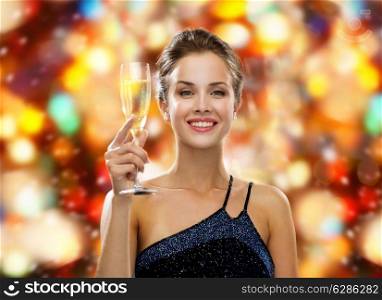 drinks, holidays, christmas, people and celebration concept - smiling woman in evening dress with glass of sparkling wine over red christmas lights background