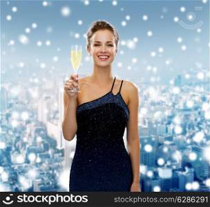 drinks, holidays, christmas, people and celebration concept - smiling woman in evening dress with glass of sparkling wine over snowy city background