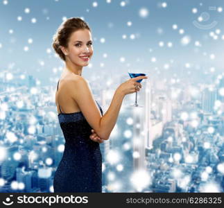 drinks, holidays, christmas, people and celebration concept - smiling woman in evening dress holding cocktail over snowy city background