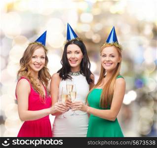 drinks, holidays, people and celebration concept - smiling women in party hats with glasses of sparkling wine over lights background
