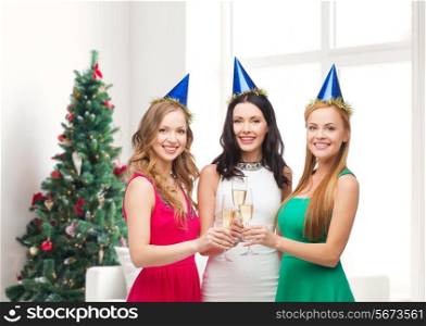 drinks, holidays, people and celebration concept - smiling women in party hats with glasses of sparkling wine over living room and christmas tree background
