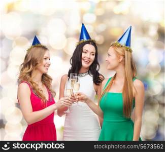drinks, holidays, people and celebration concept - smiling women in party hats with glasses of sparkling wine over lights background