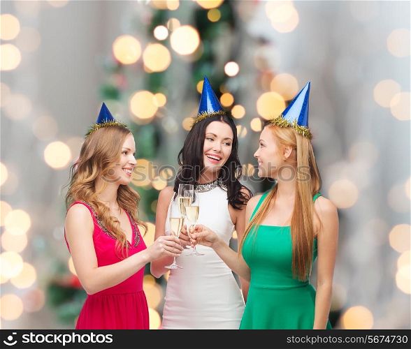 drinks, holidays, people and celebration concept - smiling women in party hats with glasses of sparkling wine over christmas tree lights background