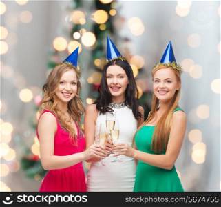 drinks, holidays, people and celebration concept - smiling women in party hats with glasses of sparkling wine over christmas tree lights background