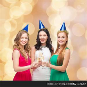 drinks, holidays, people and celebration concept - smiling women in party hats with glasses of sparkling wine over beige lights background
