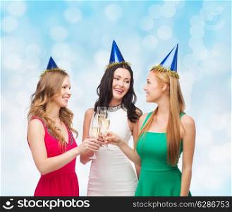 drinks, holidays, people and celebration concept - smiling women in party hats with glasses of sparkling wine over blue lights background