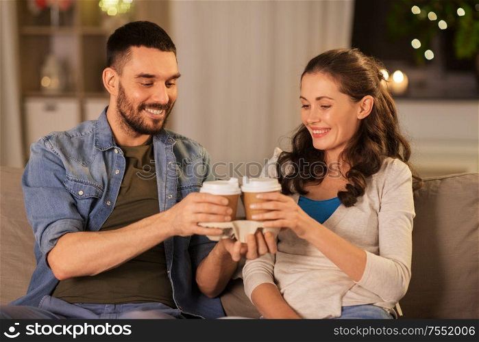 drinks, leisure and people concept - happy couple drinking takeaway tea or coffee at home in evening. happy couple drinking tea or coffee at home
