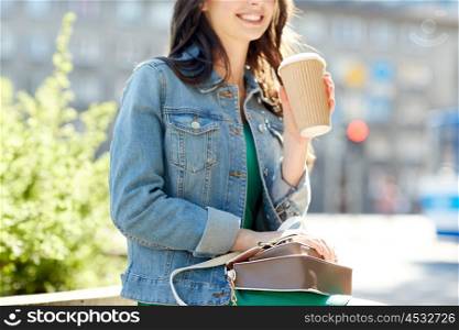 drinks, leisure, summer holidays and people concept - close up of happy young woman or teenage girl with handbag drinking coffee from paper cup sitting on on city street bench