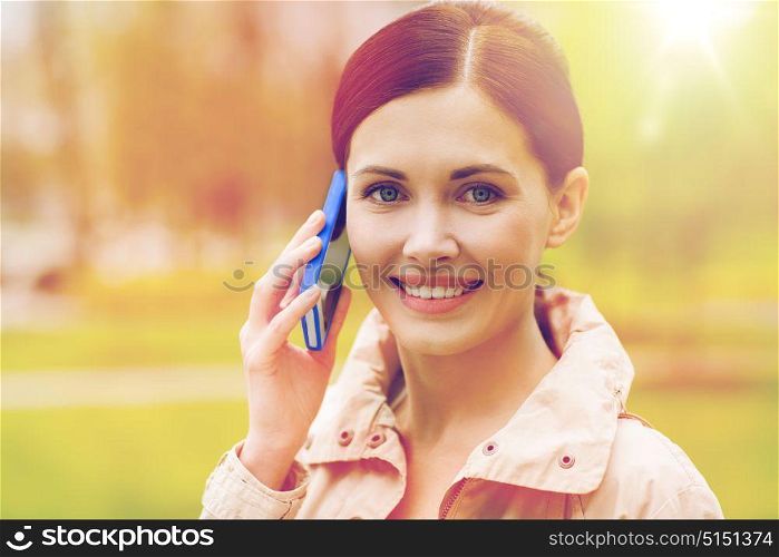drinks, leisure, technology and people concept - smiling woman calling and talking on smartphone in park. smiling woman calling on smartphone in park
