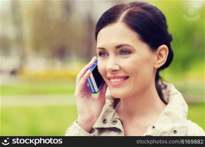 drinks, leisure, technology and people concept - smiling woman calling and talking on smartphone in park