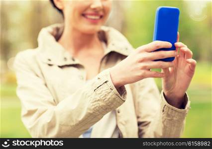 drinks, leisure, technology and people concept - smiling woman taking picture or selfie with smartphone in park