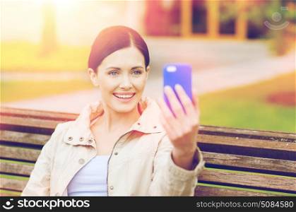 drinks, leisure, technology and people concept - smiling woman taking picture with smartphone in park. smiling woman taking picture with smartphone. smiling woman taking picture with smartphone