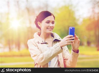 drinks, leisure, technology and people concept - smiling woman taking picture with smartphone in park. smiling woman taking picture with smartphone