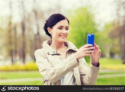 drinks, leisure, technology and people concept - smiling woman taking picture with smartphone in park