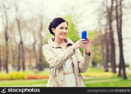 drinks, leisure, technology and people concept - smiling woman taking picture with smartphone in park