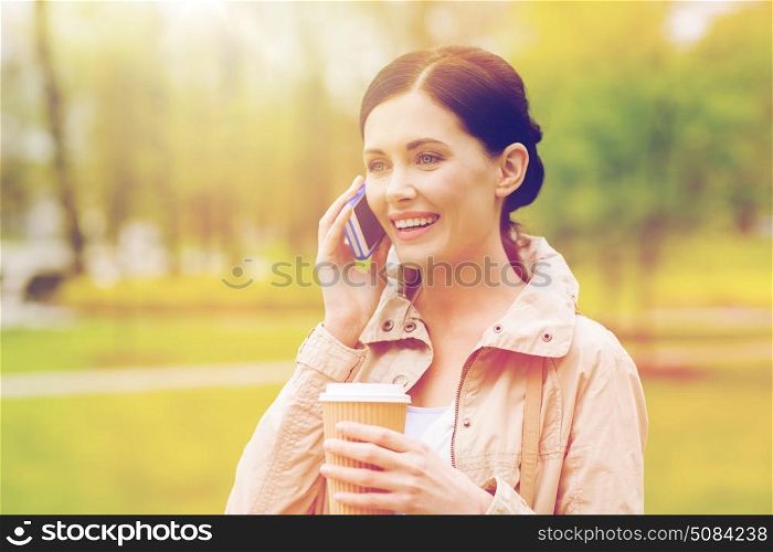 drinks, leisure, technology and people concept - smiling woman with coffee calling and talking on smartphone in park. smiling woman with smartphone and coffee in park. smiling woman with smartphone and coffee in park