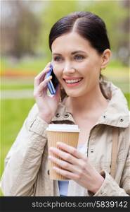 drinks, leisure, technology and people concept - smiling woman with coffee calling and talking on smartphone in park
