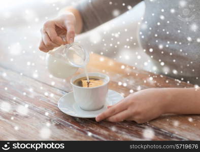 drinks, people and home concept - close up of female sitting at table and pouring milk into coffee cup