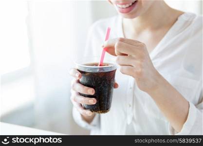 drinks, people and lifestyle concept - close up of happy woman drinking coca cola from plastic cup with straw at home