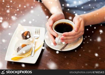 drinks, people and lifestyle concept - close up of woman hands holding cup with hot black coffee and dessert over snow