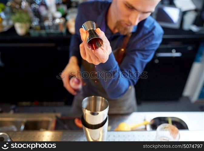 drinks, people and luxury concept - bartender pouring alcohol from jigger into shaker and preparing cocktail at bar. bartender with shaker preparing cocktail at bar