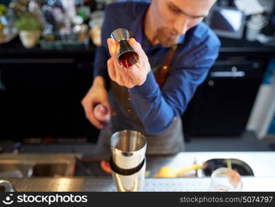 drinks, people and luxury concept - bartender pouring alcohol from jigger into shaker and preparing cocktail at bar. bartender with shaker preparing cocktail at bar