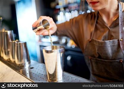 drinks, people and luxury concept - woman bartender with jigger pouring alcohol into shaker and preparing cocktail at bar counter. bartender with cocktail shaker and jigger at bar. bartender with cocktail shaker and jigger at bar