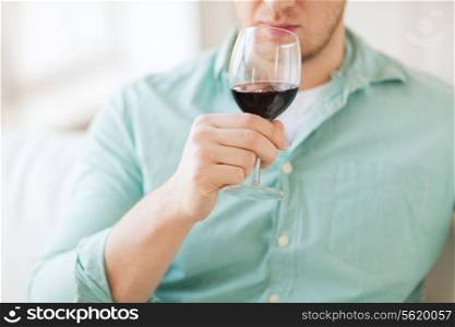 drinks, relax, leisure and people concept - close up of man drinking red wine and sitting on couch at home