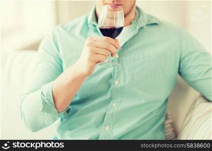 drinks, relax, leisure and people concept - close up of man drinking red wine and sitting on couch at home