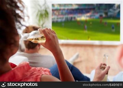 drinks, sport and leisure concept - happy woman friends drinking non-alcoholic beer and watching watching soccer or football on projector screen at home. woman drinking beer and watching soccer game. woman drinking beer and watching soccer game