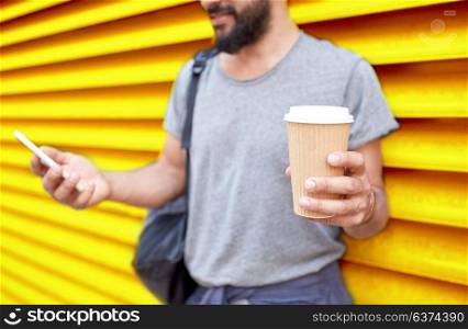 drinks, technology and people concept - close up of man with coffee cup and smartphone on street over ribbed yellow wall background. man with coffee cup and smartphone over wall
