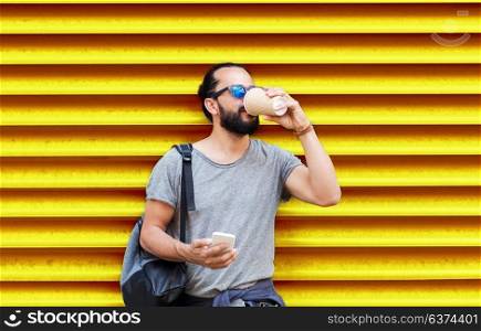 drinks, technology and people concept - man with smartphone drinking coffee from disposable paper cup on street over ribbed yellow wall background. man with smartphone drinking coffee over wall