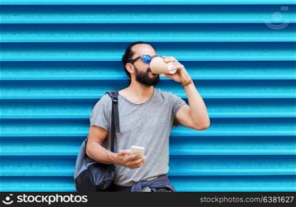 drinks, technology and people concept - man with smartphone drinking coffee from disposable paper cup on street over ribbed blue wall background. man with smartphone drinking coffee over wall