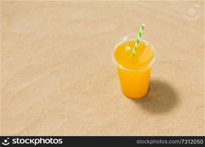 drinks, vacation and summer holidays concept - cup of orange juice with straw on beach sand. cup of orange juice with straw on beach sand