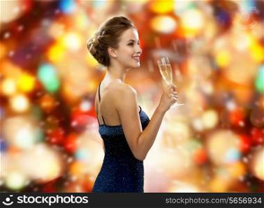 drinks, winter holidays, luxury and celebration concept - smiling woman in evening dress with glass of sparkling wine over red christmas lights background