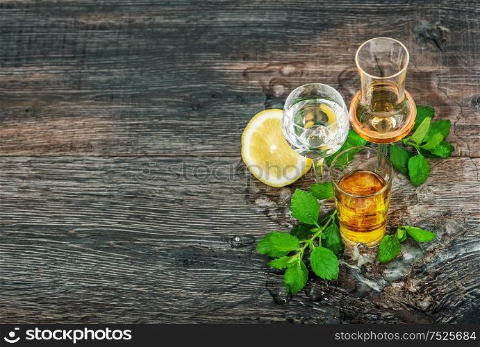 Drinks with ice, lemon, mint leaves on wooden background. Aperitif, whiskey, gin, rum, vodka