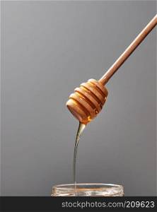Dripping sweet honey into a jar with fresh organic syrup on a gray background, place for text. Jewish rosh hashanah holiday concept.. Close up of wooden stick with dripping sweet natural honey on a gray background, traditional useful sweetness.